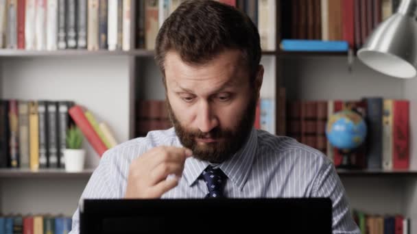 Eye fatigue, manager syndrome, exhaustion, stress, overwork, sleep disorder concepts. Tired bearded man at workplace works typing on laptop, breaks off and drips drops into his eyes. Close-up — Stock Video