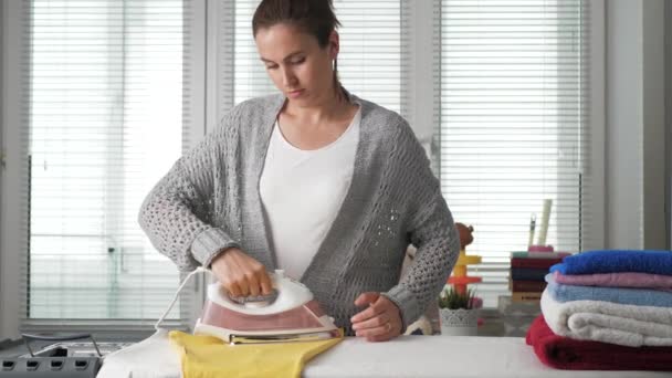 Meisjes strijken kleren. Jonge vrouw alleen in de kamer neemt ijzer en strijkt gele jurk, verwijdert ijzer en zet kleren in stapel — Stockvideo