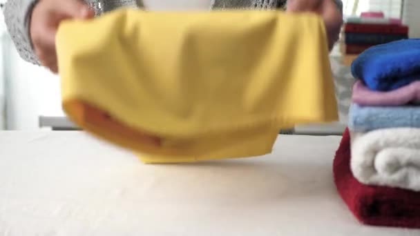 As mãos femininas empilham o vestido amarelo na pilha com a roupa passada. Conceito de roupa de engomar menina — Vídeo de Stock