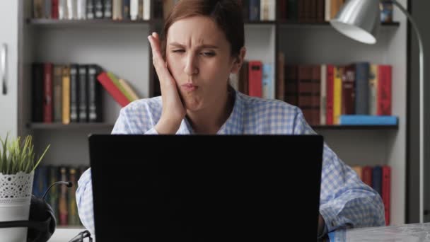 Dolor de muelas. Mujer molesta en el lugar de trabajo utiliza el ordenador portátil, tiene dolor de muelas y toca su cara con la mano. Concepto de enfermedad dental. Tiro medio — Vídeo de stock