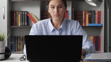 Dirsek ağrısı. Kadın bilgisayarda çalışıyor, elinde ağrı hissediyor ve üzgün, diğer eliyle dirseğine dokunuyor. Orta boy.