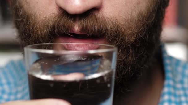 수염 이 있는 사람은 반짝 이는 식수를 마신다. 남자 손 이입에 유리를 들고 광천수를 마신다 — 비디오