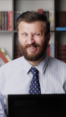 Dikey görünümlü sakallı adam ya yüz kaslarını esnetir ya da komik surat yapar. Yakın plan.
