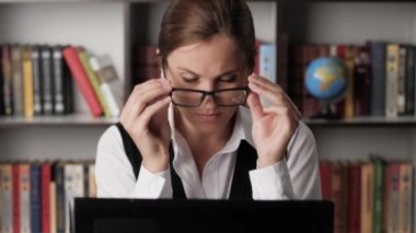 Yorgunluk ve göz ağrısı. İş yerinde gözlüklü çekici bir kadın klavyede çalışıyor, gözlüklerini çıkarıyor ve elleriyle gözlerini ovuyor. Müdür sendromu, uykusuzluk, geri dönüşüm konsepti. Yakın plan.