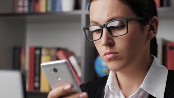 Frau, die Anrufe entgegennimmt. Arbeiterin mit Brille am Arbeitsplatz hält Handy in der Hand, blickt fasziniert auf Bildschirm, hält Smartphone ans Ohr und sagt Hallo. Nahaufnahme — Stockvideo
