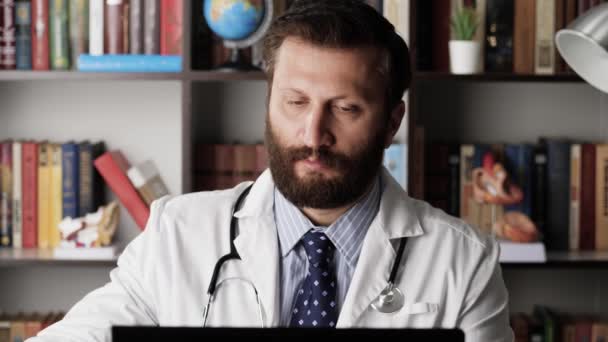 医生倒咖啡。在办公室工作的男性医生有些疲倦或困倦，他在电脑前工作，打断他从咖啡壶倒咖啡，然后在键盘上键入一些东西 — 图库视频影像