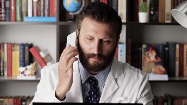 Il dottore va dal paziente. Il medico maschio in camice bianco sul posto di lavoro nell'ufficio ospedaliero risponde alla telefonata e lascia l'ufficio, possibilmente al paziente o alla riunione. — Video Stock