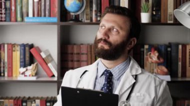 Doktor düşünüyor. Hastane ofisindeki iş yerinde beyaz önlüklü dalgın erkek doktor elinde belgeler ya da tıbbi kayıtları tutuyor, tükenmez kalemi elinde tutuyor ve karar veremiyor.