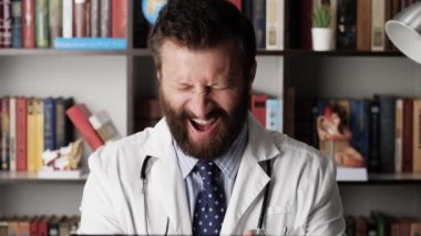 Çılgın doktor konsepti. Hastane işyerindeki beyaz önlüklü komik erkek doktor dizüstü bilgisayarda çalışırken çok garip davranıyor.