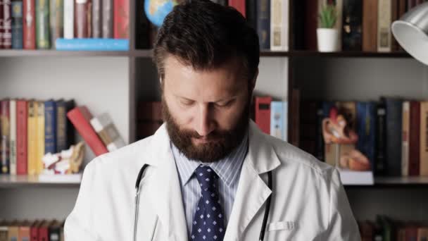Doktor zaczyna dzień pracy. Skoncentrowany poważny lekarz w białym płaszczu w miejscu pracy w biurze szpitalnym zakłada okulary na oczy i otwiera laptopa, zaczyna pisać — Wideo stockowe