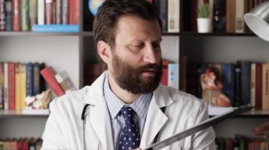 Doktor çalışanlara küfrediyor. Ciddi, odaklanmış, beyaz önlüklü erkek doktor hastane ofisinde, ona belgeler getiriyorlar, onlara bakıyor ve meslektaşlarını azarlamaya başlıyor.