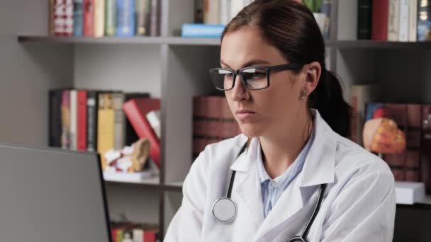 Tired doctor at computer, pain in neck, neckache. Concentrated female doctor in white coat at workplace in office works at computer, pauses and kneads tired neck — Stock Video