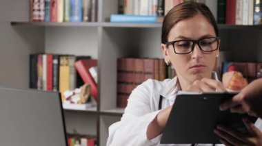 Doktor belgeleri imzalar. Ofiste çalışan beyaz önlüklü kadın bilgisayar başında çalışıyor. Belgeleri getiriyor, imzalıyor ve geri veriyor.