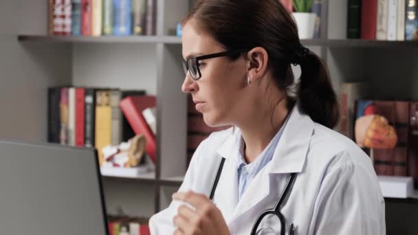 Doktor začíná pracovat. Žena lékař v bílém plášti na pracovišti v kanceláři nasadí brýle pro vidění, zvedne lékařské záznamy nebo dokumenty a začne studovat — Stock video
