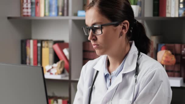疲倦的医生眼药水。办公室里穿着白衣的女医生在电脑前工作，摘下眼镜，用眼药水 — 图库视频影像