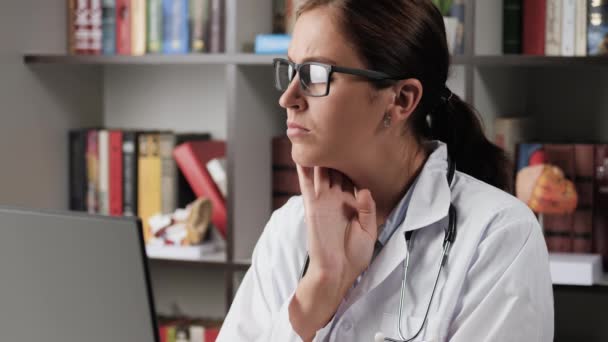 Лікар діагностує себе. Жінка-лікар в білому пальто на робочому місці в офісі відчуває пульс на шиї, потім одягає стетоскоп і слухає її серцебиття — стокове відео