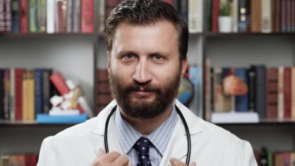 Portrait de médecin souriant. Homme sympathique médecin en manteau blanc et stéthoscope dans le bureau regarde la caméra et sourit — Video