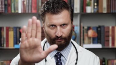 Doktor dur diyor. Beyaz önlüklü ve steteskoplu heyecanlı erkek doktor kameraya bakıyor elini kaldırıyor ve avucuyla DUR işaretini gösteriyor.