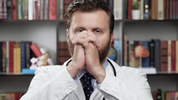 Doktor se modlí. Rozrušený lékař v bílém plášti a stetoskopu v kanceláři se podívá do kamery, zvedne ruce k obličeji a začne se modlit — Stock video