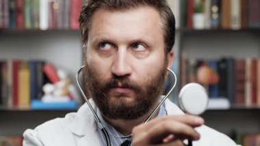 Doktor steteskop kullanıyor. Ofisteki beyaz önlüklü doktor, steteskopu elinde tutuyor ve potansiyel hastanın nefes alışını dinliyor.