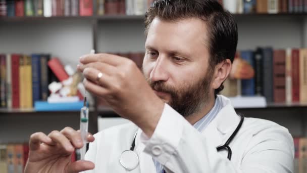 Doctor y jeringa. El doctor masculino concentrado en bata blanca en la oficina sostiene la jeringa desechable llena con solución en su mano, libera poco líquido de la jeringa y mira intrigantemente a la cámara — Vídeos de Stock