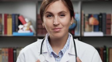 Gülümseyen doktor portresi. Beyaz önlüklü ve steteskoplu arkadaş canlısı bayan doktor kameraya bakar ve gülümser.