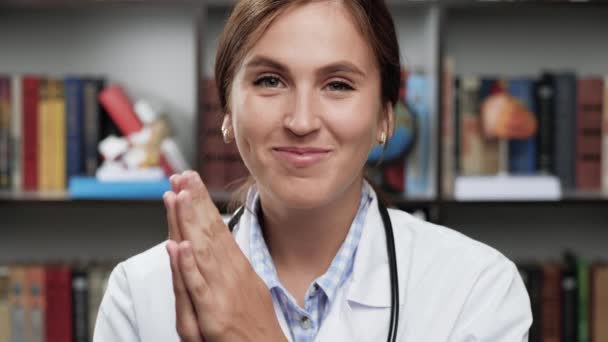 Dokter applaudisseert. Welwillende glimlachende vrouwelijke arts in witte jas en stethoscoop in het kantoor kijkt naar de camera en applaudisseert met haar handen verheugen zich in iets — Stockvideo