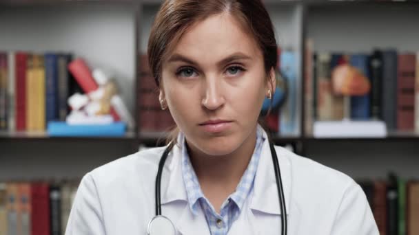 Доктор наляканий. Страшна збуджена жінка-лікар в білому пальто і стетоскоп в офісі дивиться на камеру і закриває обличчя руками — стокове відео