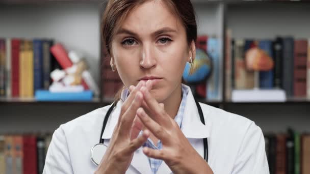 Doktorn ber. Upprörd kvinna läkare i vit rock och stetoskop på kontoret tittar på kameran, höjer händerna mot ansiktet och börjar be — Stockvideo
