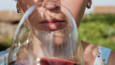 Kadın şarap içiyor. Kadın eli ağzına kırmızı şarap ile cam getirir ve doğanın güneşli bir gününde içer. Yakın plan.