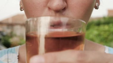 Kadın elma ya da üzüm suyu içiyor. Kadın eli ağzına elma suyu veya üzüm suyu katılmış cam getirir ve doğada güneşli bir günde onu içer. Yakın plan.