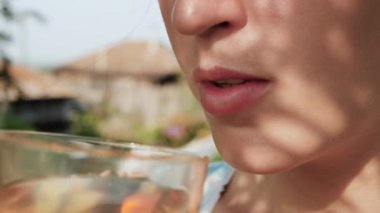 Kadın elma ya da üzüm suyu içiyor. Kadın elinin yan görünüşü, elmalı ya da üzümlü bardağı ağızlarına getirir ve güneşli bir günde içer. Yakın plan.