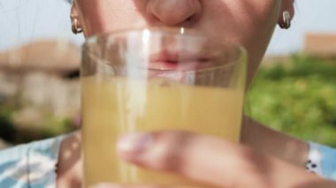 Kadın portakal suyu içiyor. Kadın eli ağzına portakal suyu katılmış bardakları getirir ve doğanın güneşli bir gününde içer. Yakın plan.