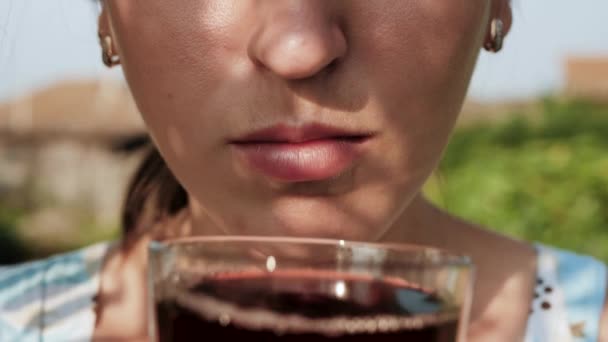 Жінка п'є вишневий або гранатовий сік. Жіноча рука приносить в рот склянку з вишневим або гранатовим соком і п'є його в сонячний день на природі. Крупним планом — стокове відео