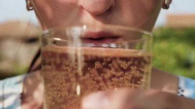 Kadın limonata içiyor. Kadın eli ağzına karbonatlı limonata ile cam getirir ve doğada güneşli bir günde içer. Yakın plan.