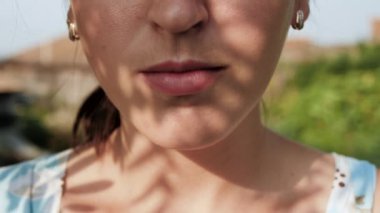 Kadın su içiyor. Kadın eli ağzına köpüklü su dolu cam getirir ve doğanın güneşli bir gününde onu içer. Yakın plan.