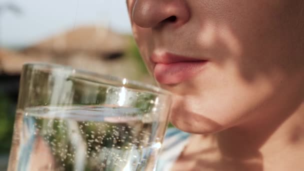La mujer bebe agua. Vista lateral de la mano femenina llevar vidrio con agua con gas a la boca y beber en el día soleado en la naturaleza. Primer plano — Vídeo de stock