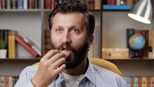 Interesse, passione, entusiasmo. L'uomo solo in camera guarda la TV la sera e mangia popcorn, è molto interessato a ciò che vede sullo schermo e non riesce a togliersi gli occhi di dosso. Primo piano — Video Stock