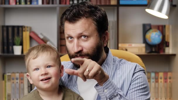 Papa en kleine baby kijken tv en eten popcorn, papa wijst met zijn vinger naar het kind, ze hebben plezier. Close-up — Stockvideo