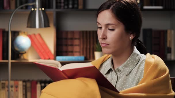 La mujer lee el libro por la noche. Grl pensativo, solo por la noche o por la noche en la habitación envuelto en manta lee libro, mira por la ventana y da vuelta la página — Vídeos de Stock