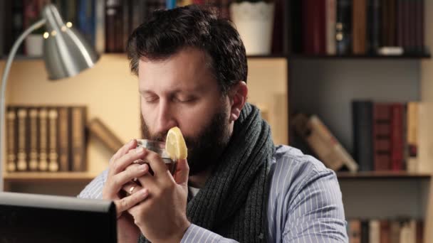 Mężczyzna z przeziębieniem powoli pije gorącą herbatę z cytryną w miejscu pracy w biurze lub mieszkaniu, jedząc kawałek cytryny. Koncepcja leczenia zimnej grypy — Wideo stockowe
