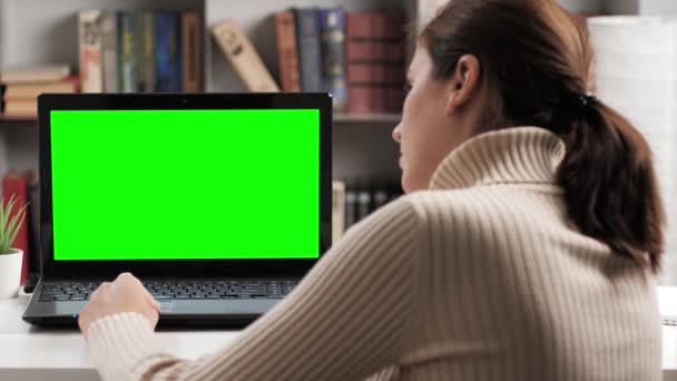 Kobieta siedząca przy stole w mieszkaniu lub biurze, patrzy na zielony ekran laptopa i uruchamia palec wskazujący na laptopie touchpad. Chroma key komputer ekranowy kobieta pracuje na komputerze — Wideo stockowe