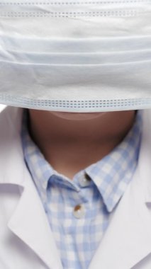 Kadın doktor yüzüne cerrahi maske takıyor. Ameliyat için hazırlık, enfeksiyonlara karşı koruma, salgın, sağlık, ilaç, virüs, grip, COVID-19, salgın konsepti. Dikey yakın çekim videosu