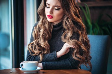 Güzel genç kadının kahve kapuçino pencere bir kafede yakınındaki köpük ile