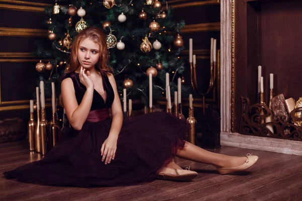 Irmãs em frente ao abeto e lareira com velas e presentes. Véspera de Ano Novo. Véspera de Natal. Férias acolhedoras no abeto com luzes e decoração dourada . — Fotografia de Stock