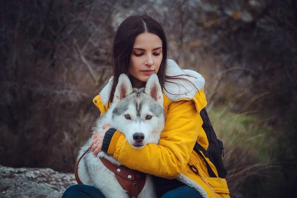 Jong vrouwtje zittend met siberische husky hond in bergen — Stockfoto