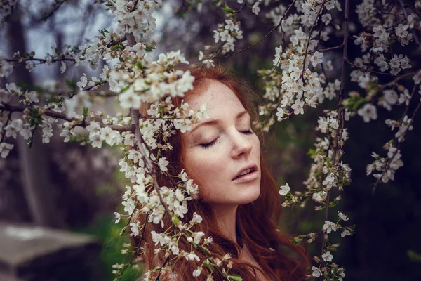 赤い髪と開花の春の庭の香りを楽しむ美しい幸せな若い女 — ストック写真