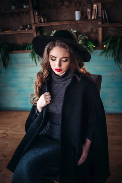 젊은 아름 다운 유행 여자 카페에서 큰 창문 가까이 앉아서 커피 한잔 들고. 세련 된 검은 모자를 착용 하는 매력적인 여자. — 스톡 사진