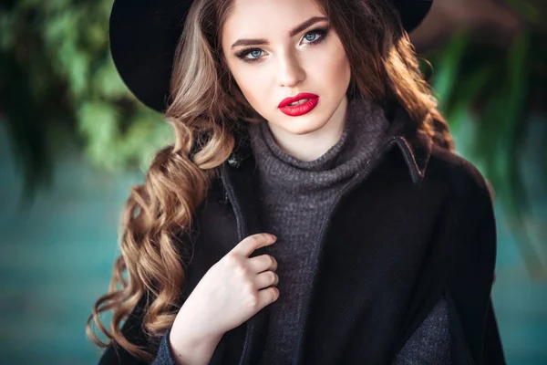 Junge schöne modische Dame sitzt in der Nähe eines großen Fensters im Café und hält eine Tasse Kaffee. attraktive Frau mit stylischem schwarzen Hut. — Stockfoto