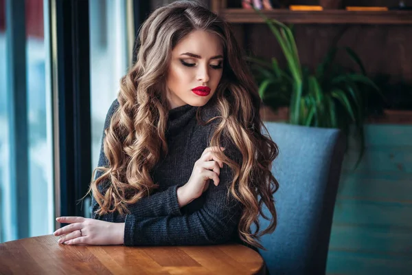 Mooie modieuze jongedame zitten in de buurt van grote venster in café en kopje koffie houden. Aantrekkelijke vrouw met stijlvolle zwarte hoed. — Stockfoto